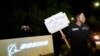 A Boeing worker wears a mask while holding a 'Happy Strike Day' sign after union members voted overwhelmingly to reject a contract offer and go on strike Sept. 13, 2024, outside the company's factory in Renton, Wash. 